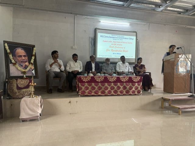 Dignitaries on the stage beside a portrait of Shri Ramakrishna Hegde